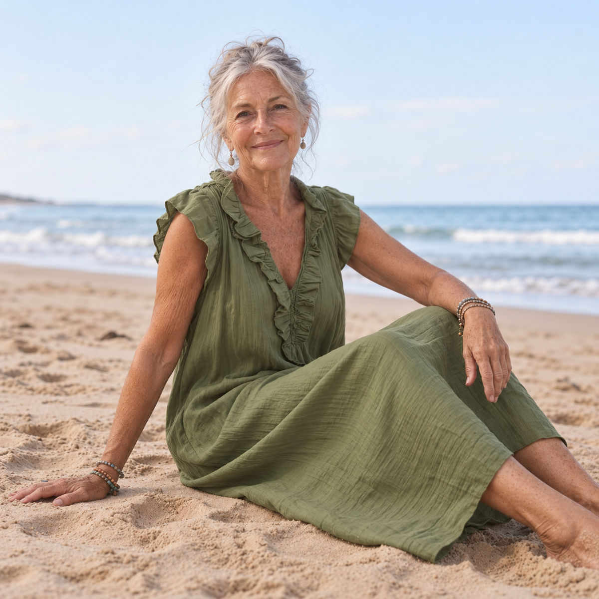 Bondi Chiara Maxi Dress in moss green with ruffled V-neck and flutter sleeves, seated on the sand